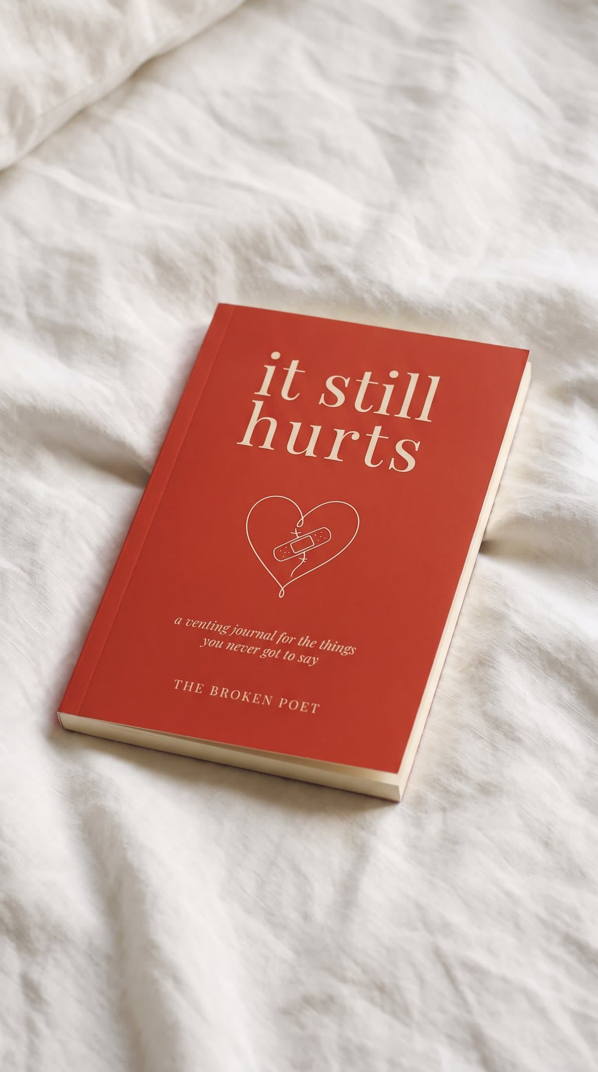 the red paperback, it still hurts, lying on white bedsheets